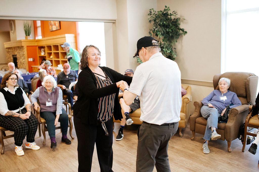 A caregiver and older gentleman dance in front of others at the Seniors Resource Center.